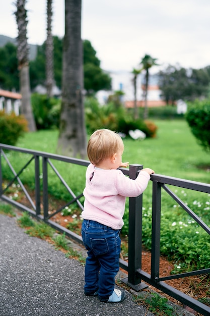 Klein meisje staat bij het hek in het park in