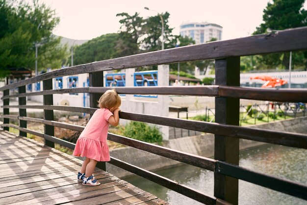 Klein meisje staat op de brug, leunend op het hek