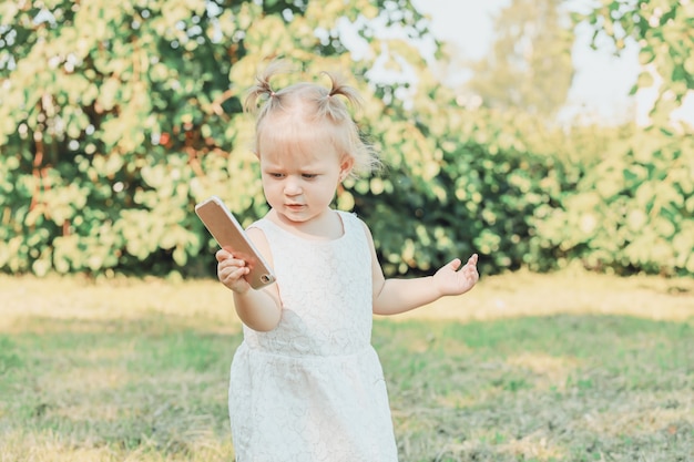 Klein meisje staat op het gras in de zomertuin met een smartphone in haar handen. hoge kwaliteit foto