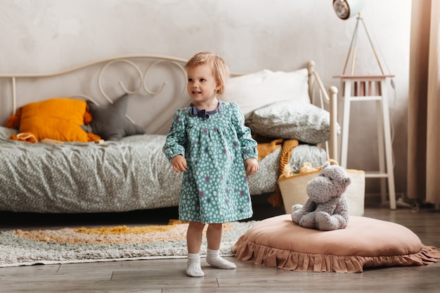 Klein meisje Todler in jurk speelt in de kinderkamer. Zachte pastelkleuren. Kinderkamer interieur bij daglicht