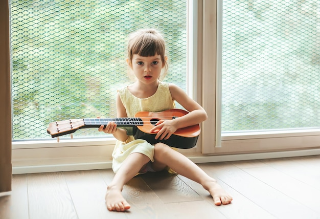 Klein meisje van 45 jaar dat zingt en ukelele speelt Mooi kind dat leert zingen en een muziekinstrument bespeelt