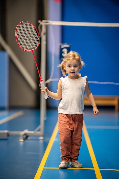 Klein meisje van drie jaar dat badminton speelt in sportkleding op de binnenbaan