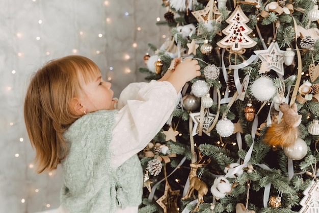 Klein meisje versiert de kerstboom met speelgoed. Een schattige baby bereidt zich thuis voor op de viering van Kerstmis.