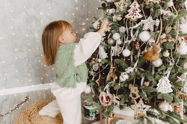 Klein meisje versiert de kerstboom met speelgoed. Een schattige baby bereidt zich thuis voor op de viering van Kerstmis.