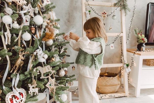 Klein meisje versiert de kerstboom met speelgoed. Een schattige baby bereidt zich thuis voor op de viering van Kerstmis.