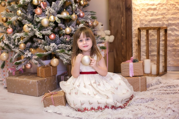 klein meisje versiert een kerstboom in de woonkamer met speelgoed