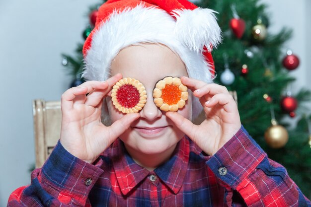 Klein meisje verwent zich met koekjes tegen de achtergrond van een kerstboom