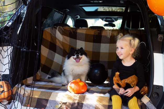 Klein meisje viert halloween plezier in de kofferbak van een hond in de buitenlucht