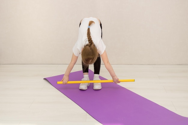 Klein meisje voert oefeningen uit met een gymnastiekstok die bukt met een stok in haar handen