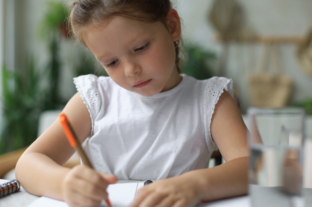 Klein meisje zit aan het bureau, schrijft in notitieblok, doet oefeningen thuis, klein kind handschrift bereidt huiswerk voor.