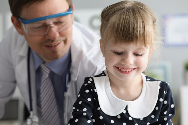 Klein meisje zit bij bezoek van man arts in kliniek