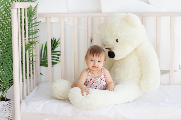 Klein meisje zit in bedje thuis met een grote teddybeer