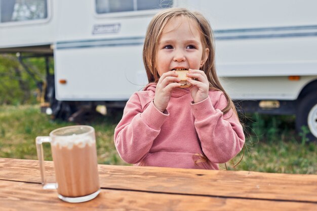 Klein meisje zit in de buurt van de camper en eet een smores gemaakt van koekjes en geroosterde marshmallows