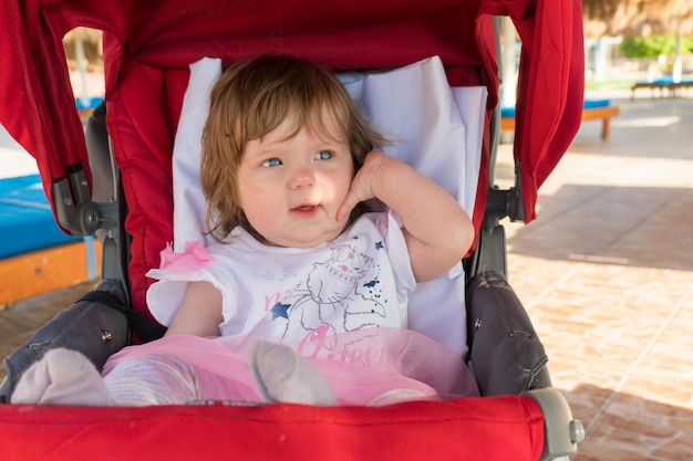 Klein meisje zit in een kinderwagen op een zonnige zomerdag