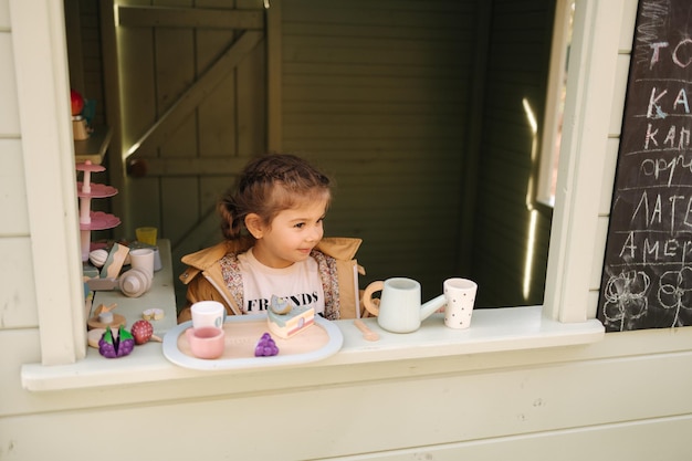 Klein meisje zit in een speelgoedcafé, gelukkig kind speelt met speelgoed buiten, kleine speelgoedstad voor