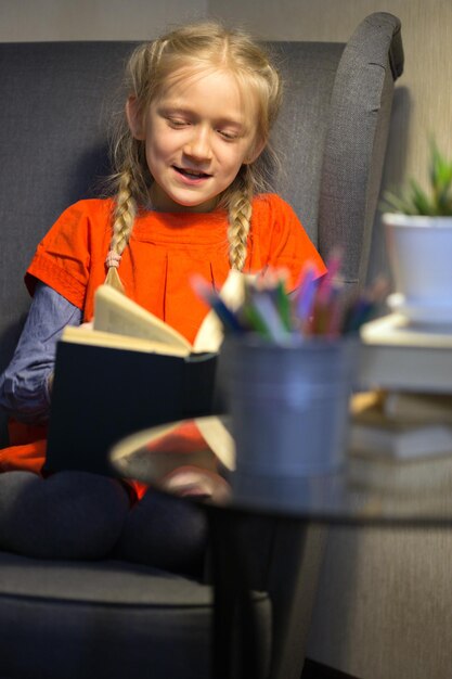 Klein meisje zit in een stoel en leest een boek