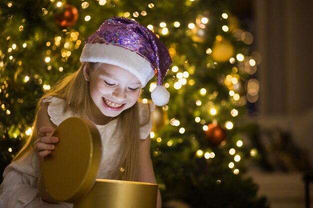 Klein meisje zit in ingerichte kerstkamer magische geschenkdoos met licht erin openen