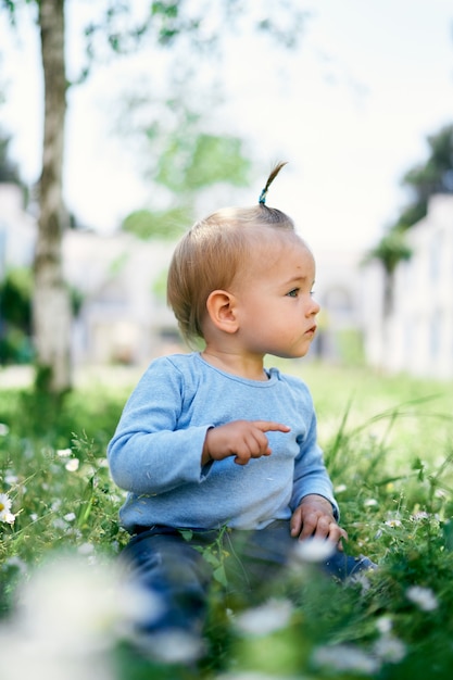 Klein meisje zit op groen gras en wijst met haar vinger in de verte