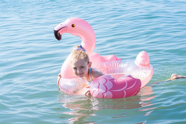 Klein meisje zwemt met een cirkel in de vorm van een flamingo in de zee