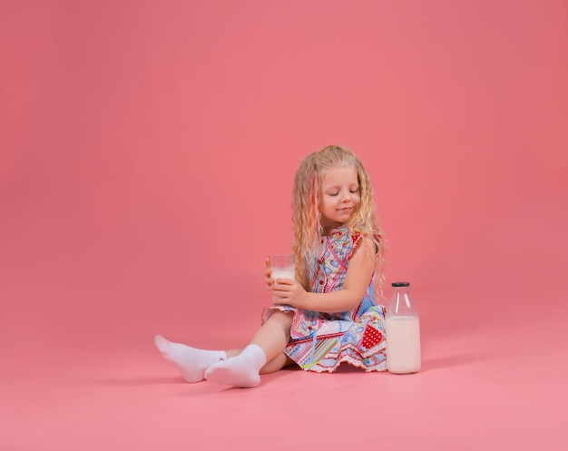 klein mooi blond meisje met melk op roze achtergrond