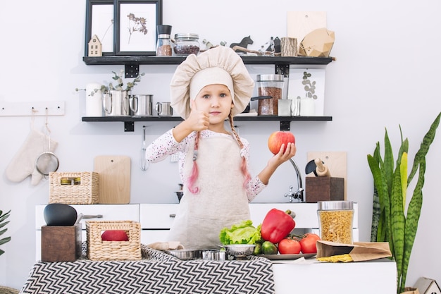 Klein mooi kindmeisje kookt in de keuken met verschillende groenten en spaghetti