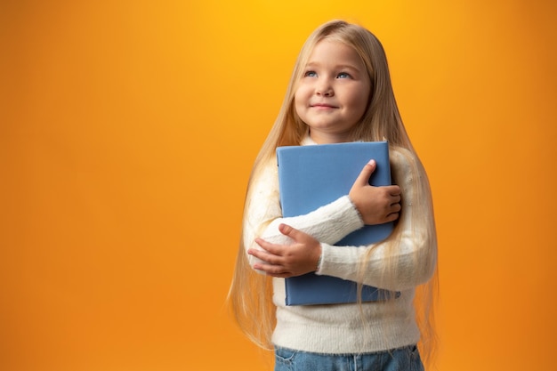 Klein mooi lachend meisje met boek tegen gele achtergrond