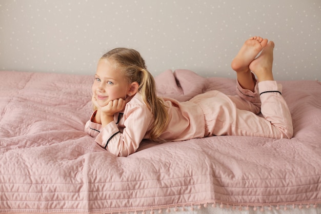 Foto klein mooi meisje in roze pyjama ligt thuis op een roze deken op het bed