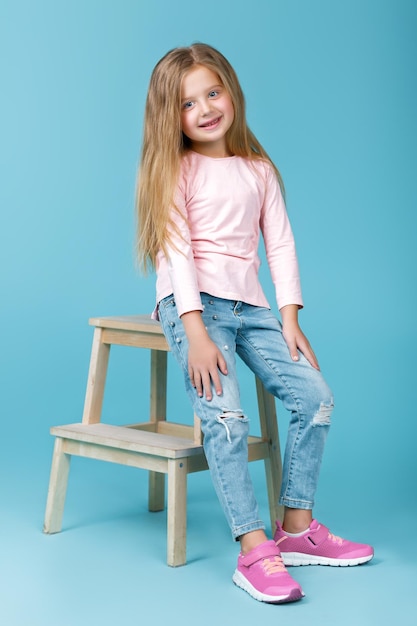 Klein mooi meisje in roze trui en jeans poseren in studio