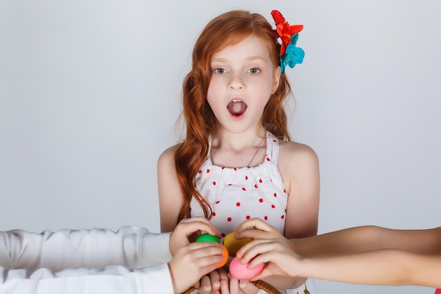 Foto klein mooi meisje zit met een mand met paaseieren en houdt paaseieren in haar handen