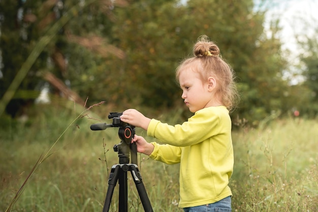 klein nieuwsgierig meisje speelt met een statief voor foto's in het park tijdens het warme seizoen