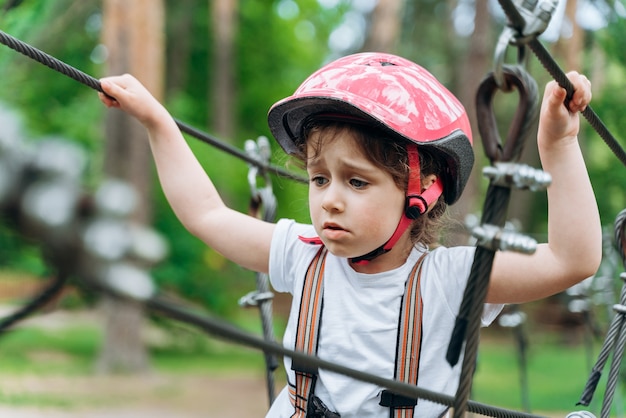 Klein, opgewonden meisje met een beschermende helm maakt zich zorgen als ze de kabelbaan passeert. schattige baby maakt zich zorgen