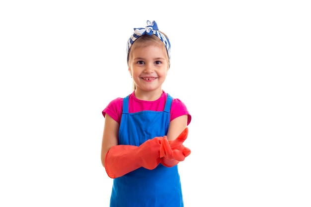 Klein optimistisch meisje met paardenstaart in roze shirt en blauwe schort met rode handschoenen in studio