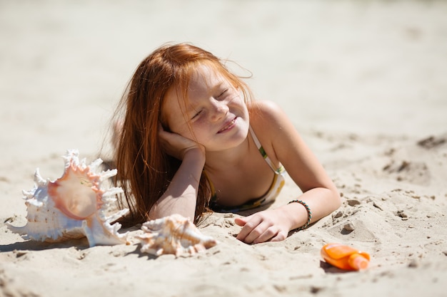 klein roodharig meisje liggend op het zand zonnebaden