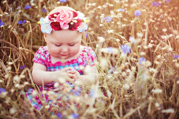 Klein schattig babymeisje met een bloemenkrans zittend op een zomerbloeiende weide