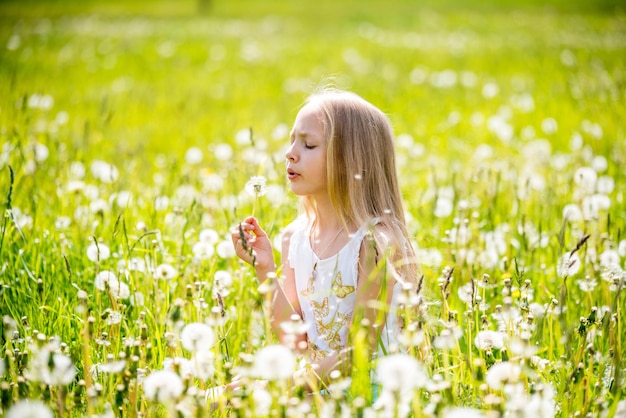 Klein schattig blond meisje met paardebloem in witte weide