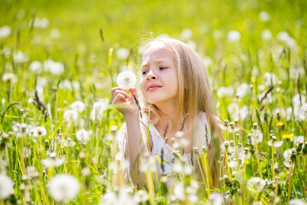 Klein schattig blond meisje met paardebloem in witte weide