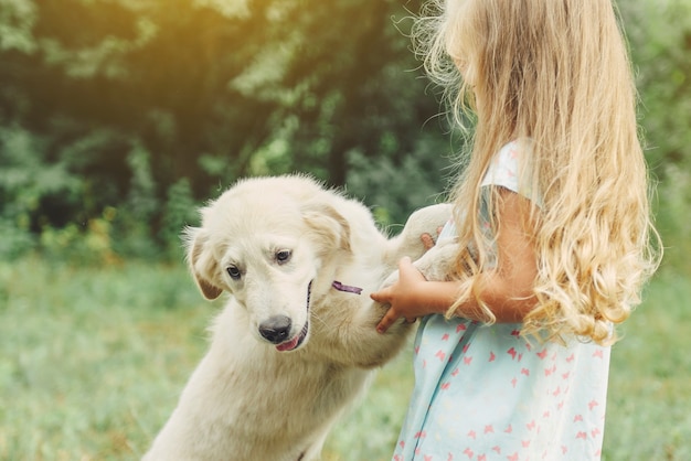 Klein schattig blond meisje speelt met haar puppy golden retriever in de zomer in het park.