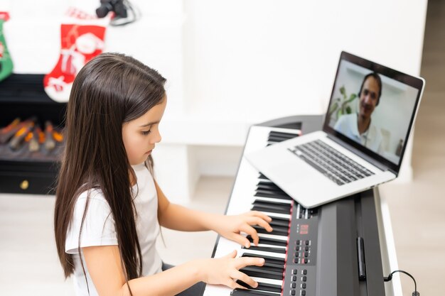 Klein schattig kindmeisje dat piano speelt met versierde kerst op de achtergrond. Kerstviering tijdens de pandemie