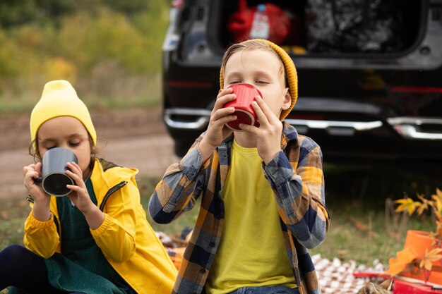 Klein schattig lachend meisje en jongen zitten in de buurt van de auto op plaid en cacao drinken Kid rust met haar familie in de natuur picknick herfstseizoen