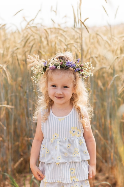 Klein schattig lachend meisje met een krans van bloemen op haar hoofd in de zomer in de natuur