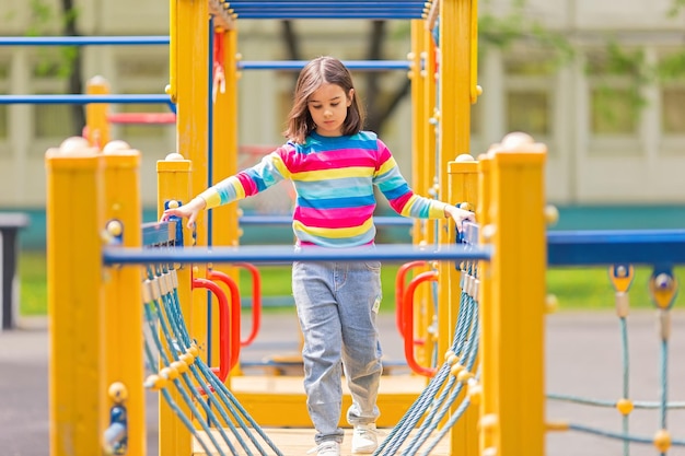 Klein schattig meisje 56 jaar oud op een kinderladder op een felgele speelplaats