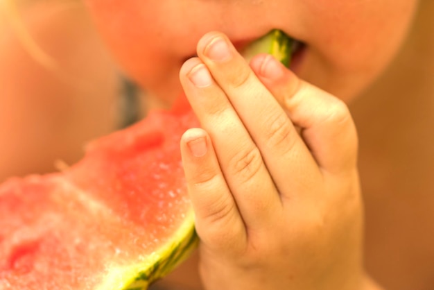 Klein schattig meisje dat een plakje rode watermeloen eet op onscherpe achtergrond Close-up zonnig