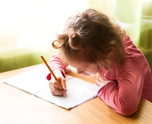 Klein schattig meisje dat haar huiswerk in werkboek schrijft
