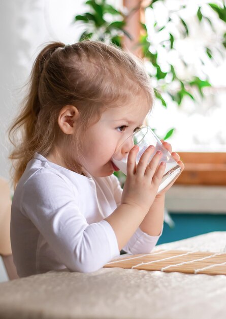 Klein schattig meisje dat melk drinkt, kind aan het ontbijt met een glas warme melk in de ochtend