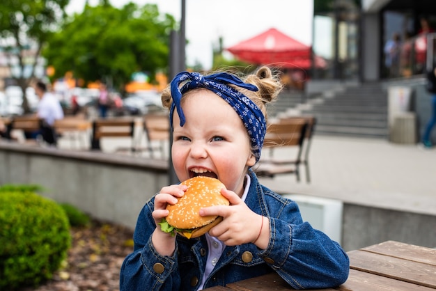 Klein schattig meisje een hamburger eten in een café. Concept van een fastfoodmaaltijd voor kinderen