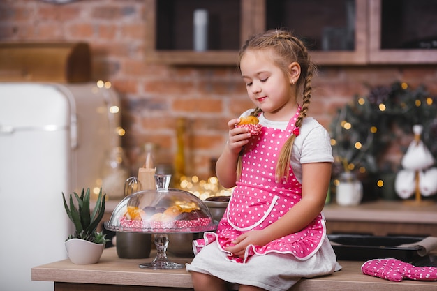 Klein schattig meisje in de keuken eten cupcakes