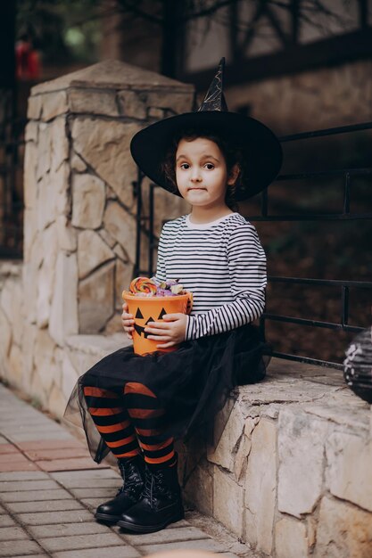 Klein schattig meisje in heksenkostuum met jackolantern-pompoenemmer met snoep en snoep Kid trick or treat in Halloween-vakantie