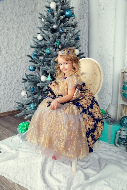 Klein schattig meisje in prinses jurk in de buurt van de boom van het nieuwe jaar, prachtige kerst decor