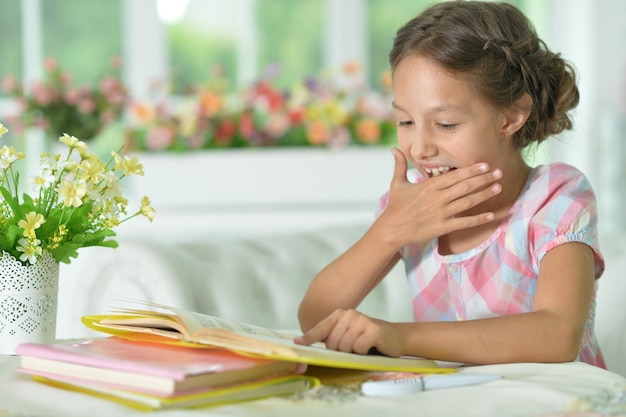 Klein schattig meisje leesboek aan tafel thuis