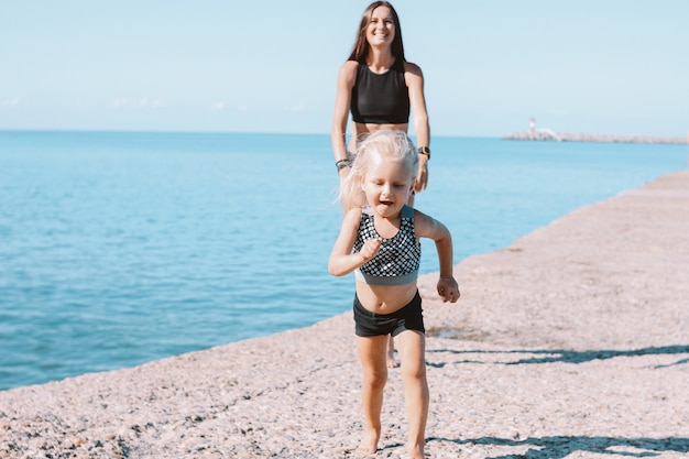 Klein schattig meisje loopt van fit moeder op strand